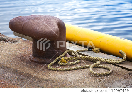Old rusted mooring bollard with naval rope on concrete pier 10097459