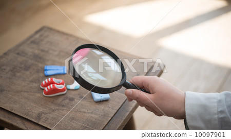 一隻手正用放大鏡觀察微型鞋子。 一隻手正用放大鏡觀察微型鞋子。 10097901