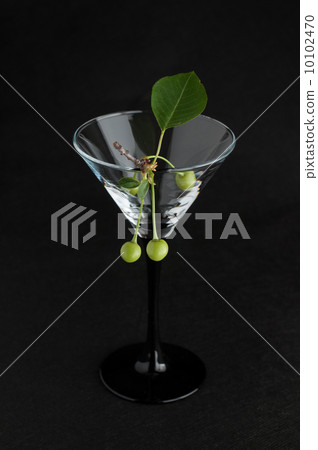 Unripe green cherry in martini glass on black 10102470