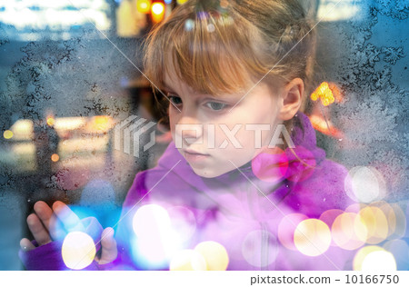 Little blond girl looks through frozen shop window glass with colorful blurred lights 10166750