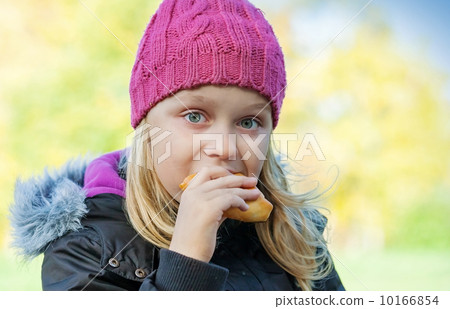 little beautiful blond girl eating cake in autumnal park. Outdoor portrait. little beautiful blond girl eating cake in autumnal park. Outdoor portrait. 10166854