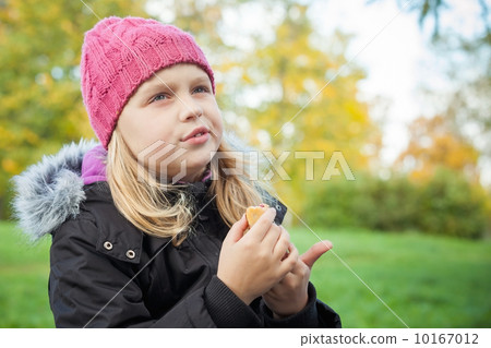 little beautiful blond girl eating cake and thinking about something. Outdoor portrait. 10167012