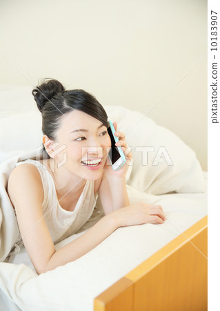 A woman talking on a smartphone while entering the bed A woman talking on a smartphone while entering the bed 10183907
