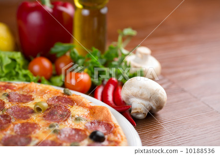 Salami pizza on table with vegetables and empty room 10188536
