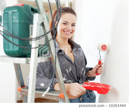 woman in grey shirt paints wall with roller 10263484