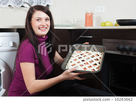 Smiling woman putting fish pie on roasting pan into oven 10263662