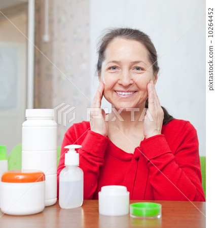 mature woman  puts cream on face at home interior 10264452
