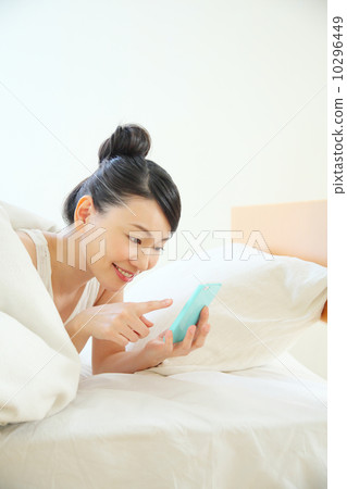 A woman using a smartphone while entering the bed 10296449