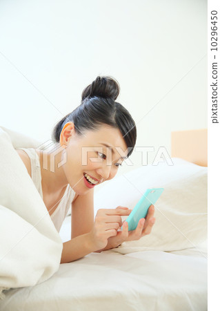 A woman using a smartphone while entering the bed 10296450