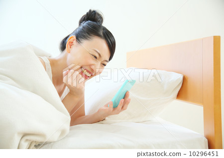 A woman using a smartphone while entering the bed A woman using a smartphone while entering the bed 10296451