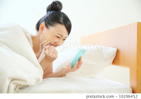 A woman using a smartphone while entering the bed 10296452