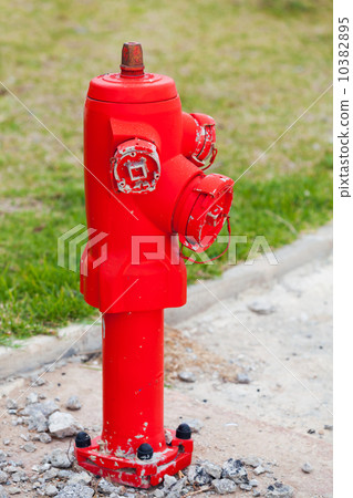 Red fire hydrant stands on the roadside with green grass 10382895