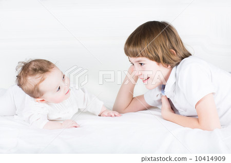 Brother and baby sister playing on a white bed Brother and baby sister playing on a white bed 10414909