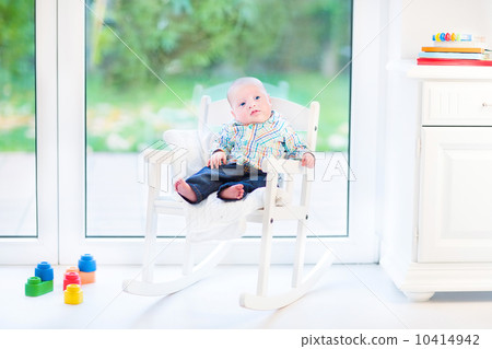 Funny newborn baby boy in a white rocking chair next to a big wi 10414942