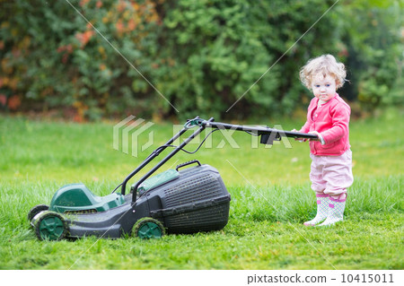 Cute toddler girl with a lawnmower in the garden 10415011