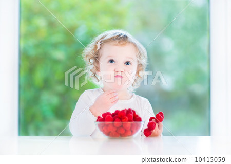 Funny baby girl eating raspberry at a white dining table next to Funny baby girl eating raspberry at a white dining table next to 10415059