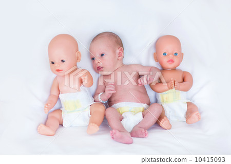 Funny newborn baby in a diaper between two plastic dolls on whit 10415093