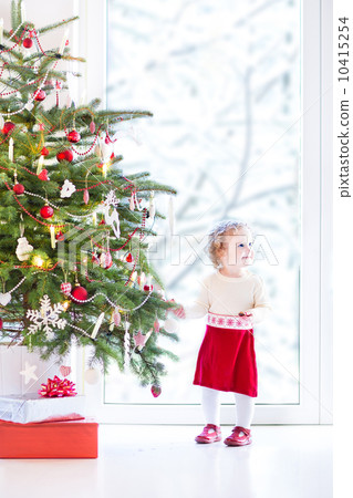 Adorable toddler girl in a warm knitted dress decorating a beaut 10415254