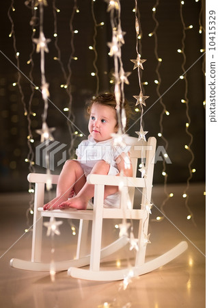 Adorable toddler girl in a white dress sitting in a white rockin 10415329