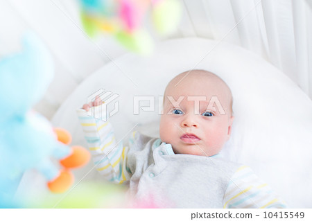 Cute little newborn baby in a white crib with colorful toys 10415549