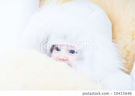 Baby girl in a white fur jacket sitting in a stroller with a warm sheepskin foot muff Baby girl in a white fur jacket sitting in a stroller with a warm sheepskin foot muff 10415646