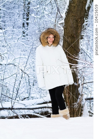 Beautiful young woman in a warm white jacket walking in a snowy 10415659