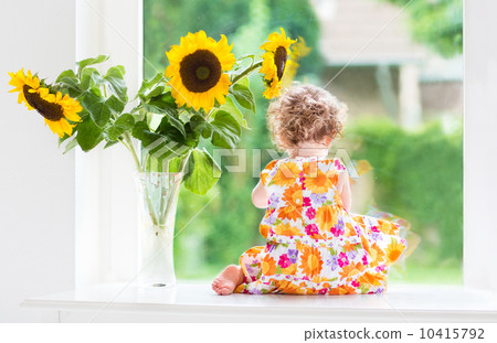 Cute curly baby girl watching out of a window into the garden si Cute curly baby girl watching out of a window into the garden si 10415792