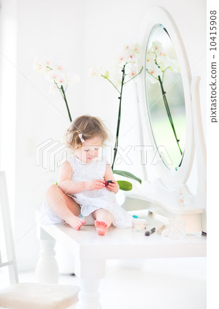Pretty toddler girl with curly hair wearing a white dress playin 10415908