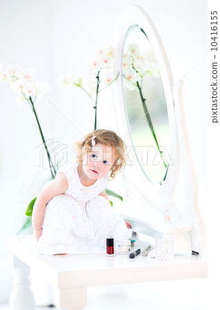 Happy toddler girl with curly hair wearing a white dress playing 10416155