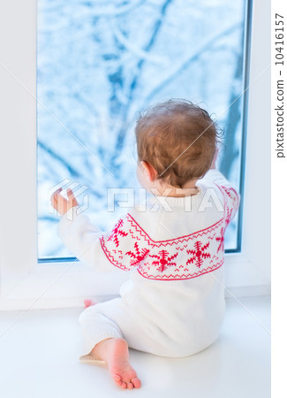 Little baby watching out of a window to a snowy garden on Christ 10416157
