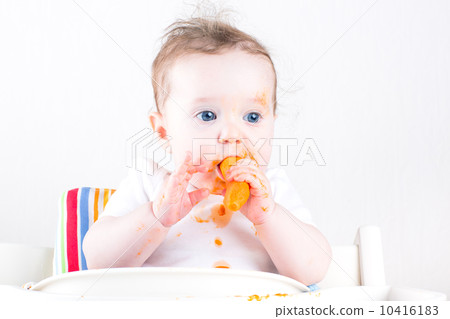 Sweet little baby eating a carrot in a white high chair 10416183