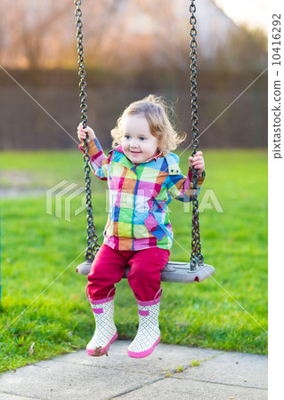 Happy laughing baby girl having fun on a swing in the garden on 10416292