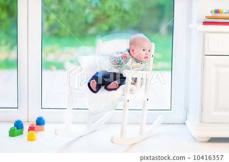Funny newborn baby boy relaxing in a white rocking chair at a bi 10416357