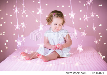 Cute toddler girl with curly hair in a white dress playing in a 10416871