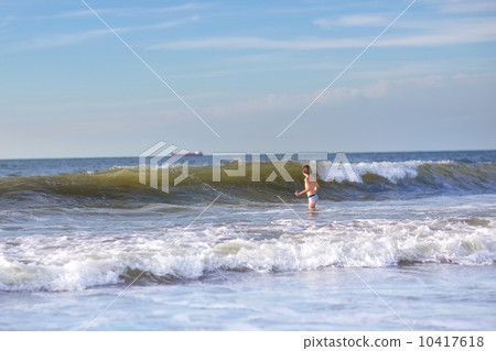 Cute boy playing with huge waves in a stormy sea on a clear sunn 10417618
