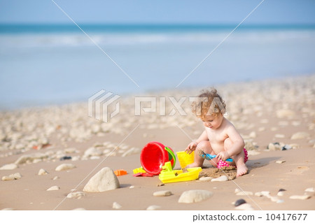 Cute curly baby girl playing with sand on a beautiful beach 10417677