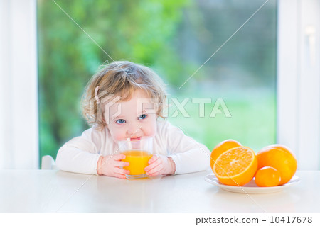 Cute little toddler girl drinking orange juice sitting at a whit Cute little toddler girl drinking orange juice sitting at a whit 10417678