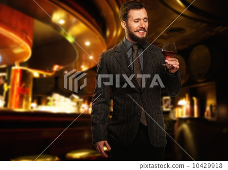 Handsome well-dressed man in jacket with glass of beverage in restaurant interior Handsome well-dressed man in jacket with glass of beverage in restaurant interior 10429918