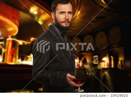 Handsome well-dressed man in jacket with glass of beverage in restaurant interior Handsome well-dressed man in jacket with glass of beverage in restaurant interior 10429920