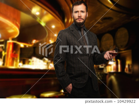 Handsome well-dressed man in jacket with glass of beverage in restaurant interior Handsome well-dressed man in jacket with glass of beverage in restaurant interior 10429922