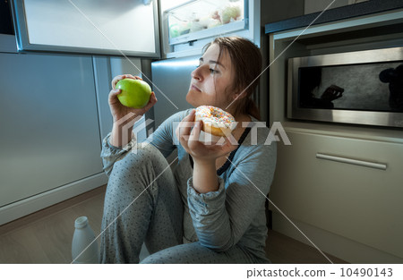 woman choosing between apple and donut at evening lunch woman choosing between apple and donut at evening lunch 10490143
