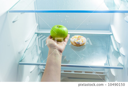 women hand holding apple instead of donut in refrigerator women hand holding apple instead of donut in refrigerator 10490150