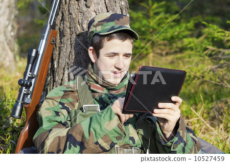 Young recruit with tablet PC and optical rifle in forest Young recruit with tablet PC and optical rifle in forest 10527459