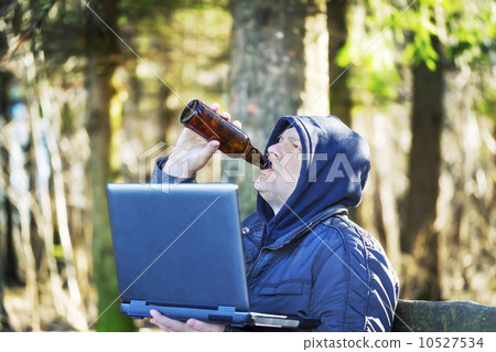 Man with beer bottle and PC in the park on a bench 10527534