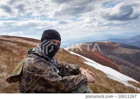 man with closed face and camouflage clothing sitting on a mounta 10611267