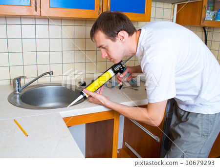 Plumber putting a silicone sealant to installing a kitchen sink 10679293