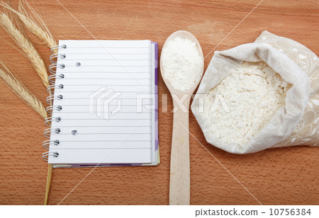 Recipe Book and flour in a sack with a spoon on a wooden table. 10756384