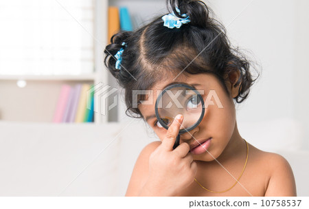 Indian girl peers at the camera through a magnifying glass 10758537