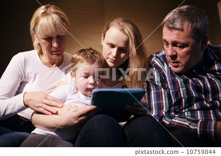 Family watching boy playing game on touchpad Family watching boy playing game on touchpad 10759844