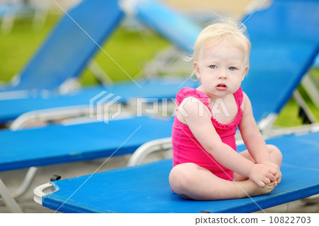 Toddler girl sitting on a sunbed by a pool 10822703